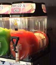 Load image into Gallery viewer, An Icm8 slushie maker with two dispensers, one filled with green slushie and the other with red slushie, under a black lid with pink and white branding.
